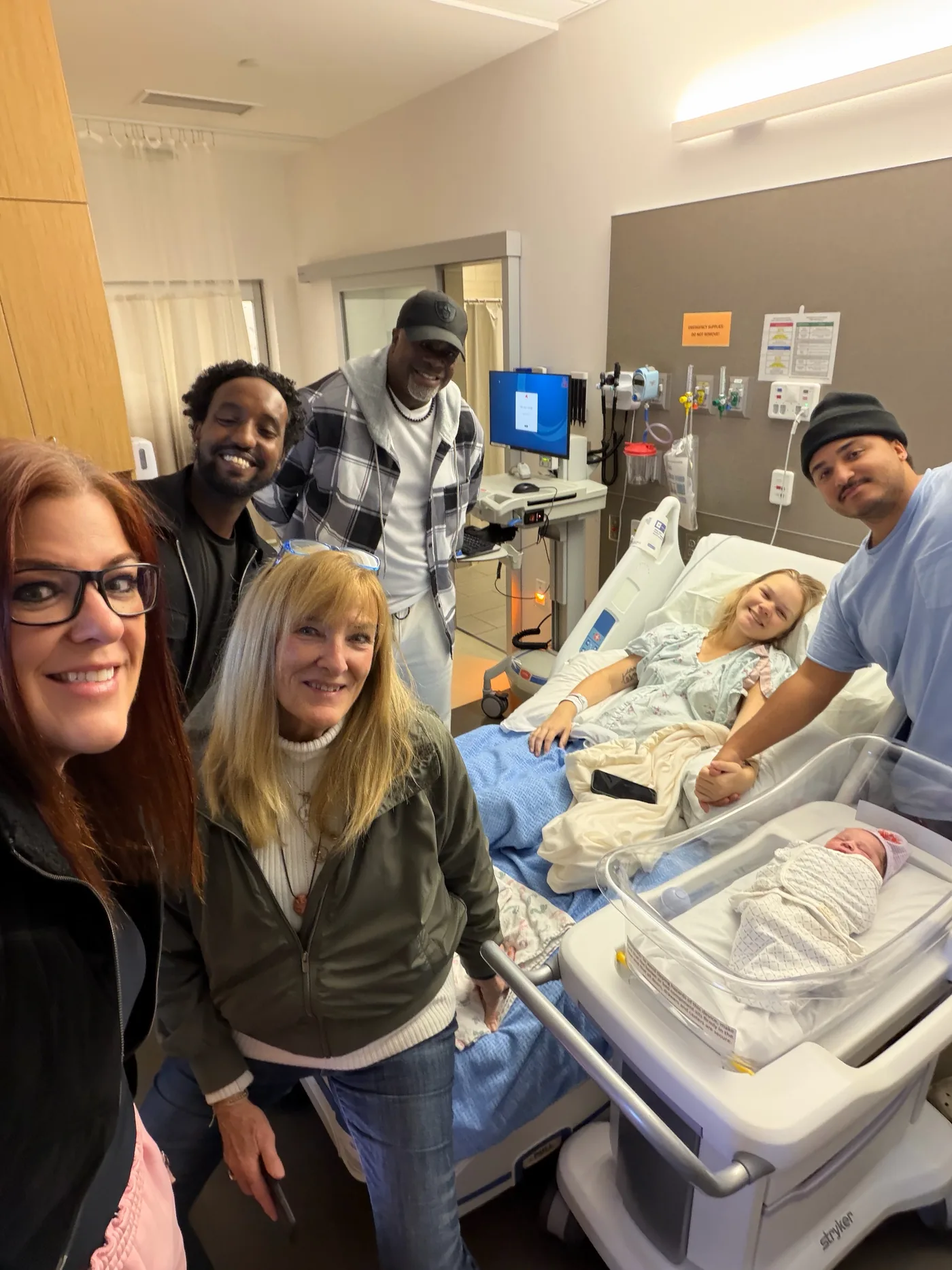 October 19, 2025. The day Dallas was born. — From left: me, Allula, Mike, Linda, Liz, Dallas, Torel. — Six years and thirteen days after my mother stood next to my father in a different hospital, — she stood next to her granddaughter holding her great-grandson. — The line continued.